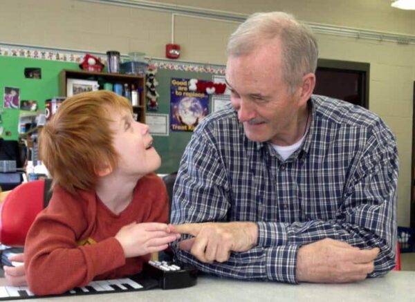 Photo a man and a young boy working at a classroom table and touching fingers while smiling